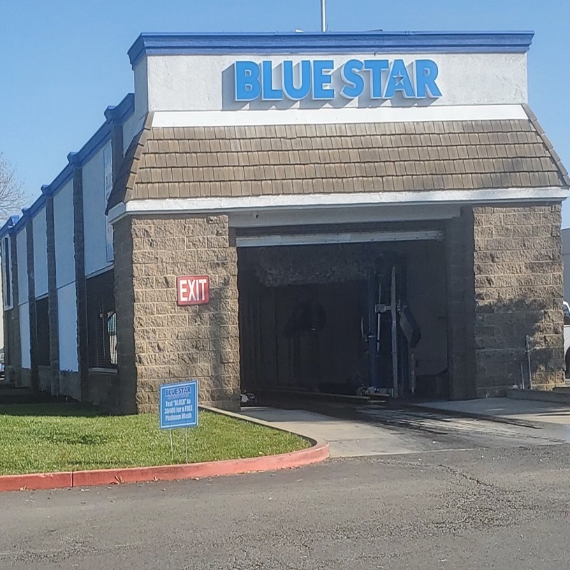 Front of the Blue Star Xpress Wash tunnel building in Elk Grove, with the blue Blue Star sign above the wash bay and a curbside yard sign offering a free Platinum wash